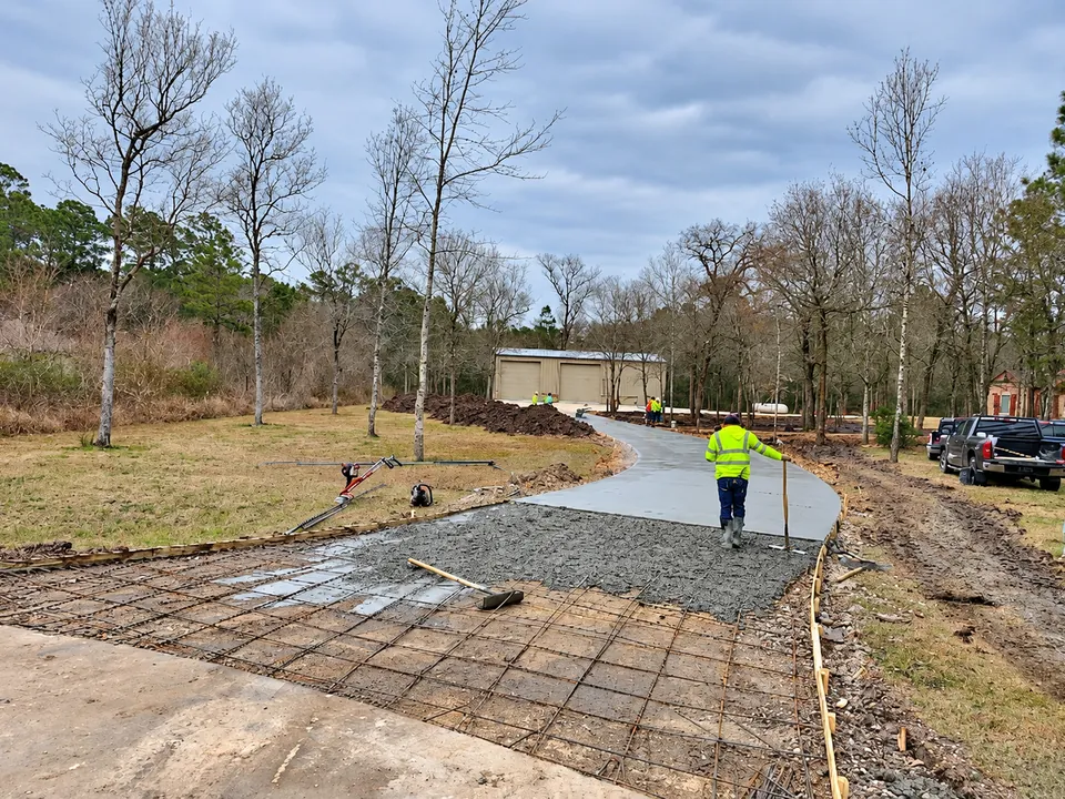 Concrete driveway being poured toward a metal building with two roll-up doors