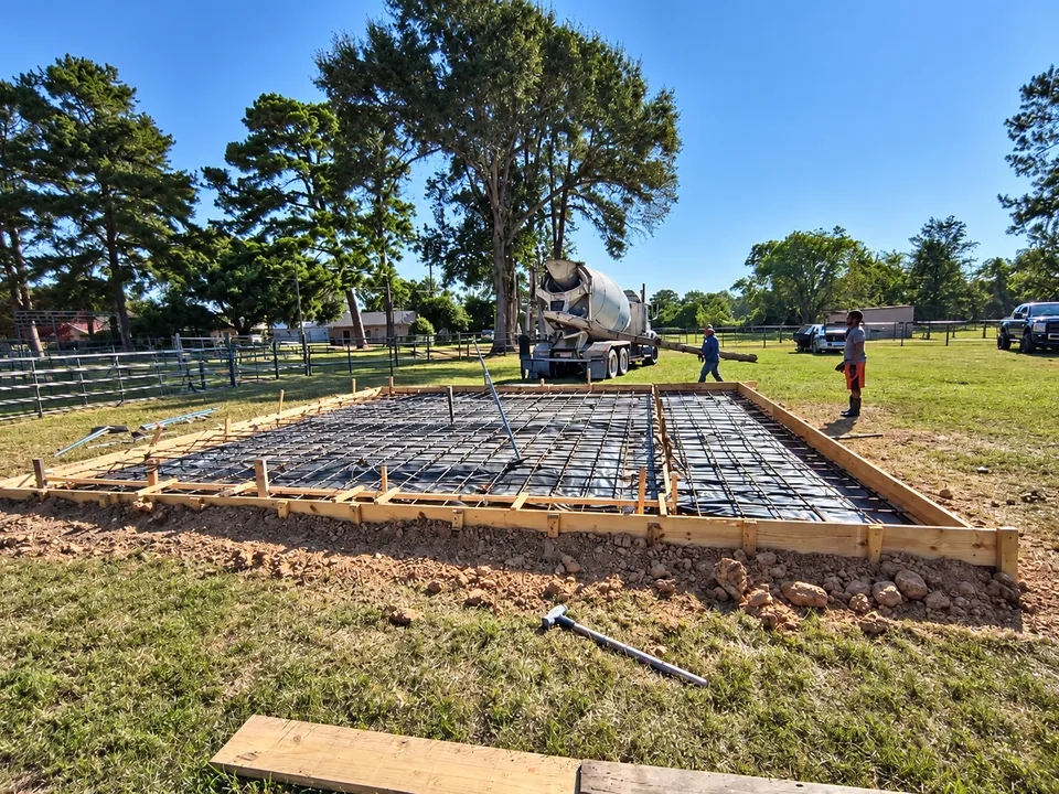 Wood forms and rebar over a vapor barrier, with a concrete truck arriving